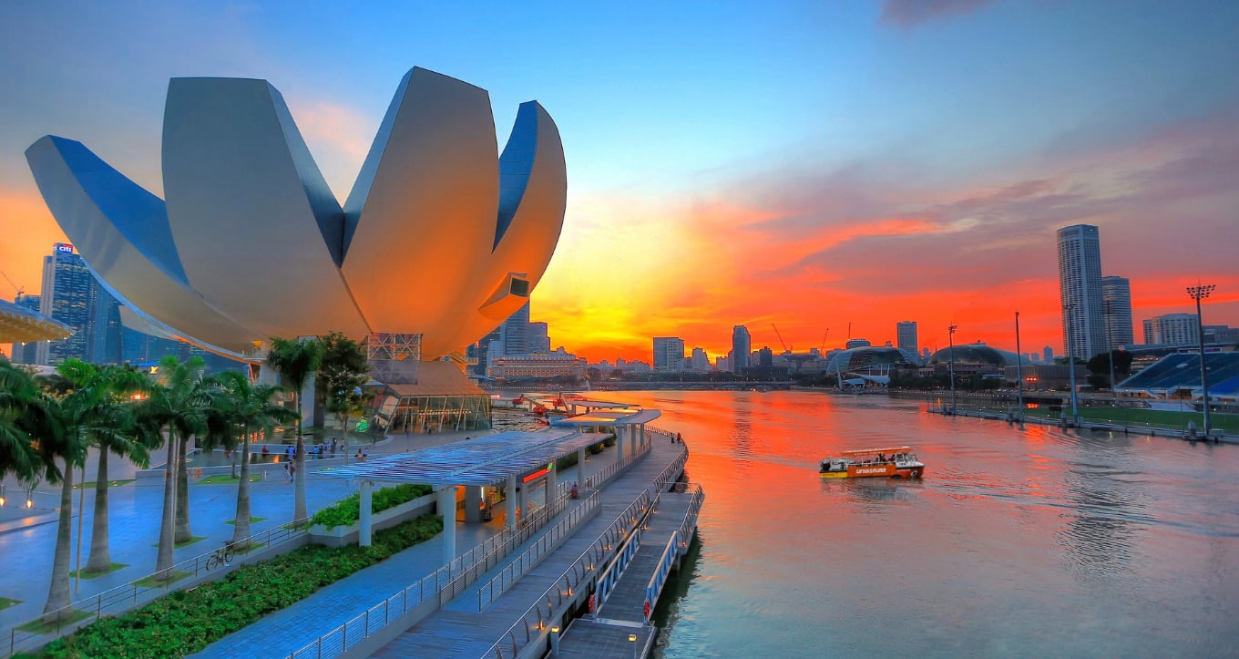A Captain Explorer DUKW amphibious vehicle cruising across Marina Bay, Singapore, at sunset with the Marina Bay Sands, Gardens by the Bay, and Singapore Flyer in the background.