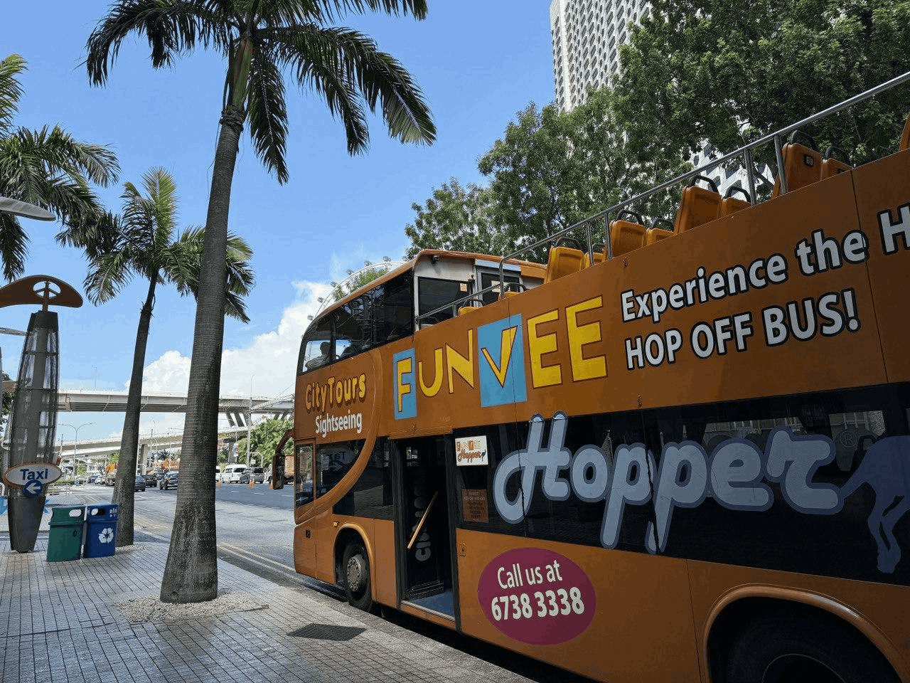 The orange City Tours FunVee open-top sightseeing bus parked next to palm trees on a sunny day in Singapore, ready for a tour.
