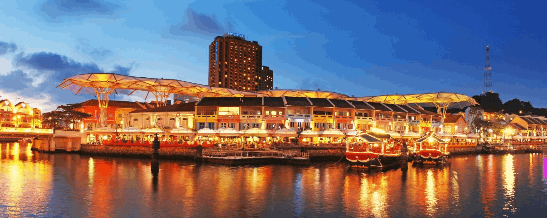 Vibrant Clarke Quay waterfront with colourful lights and river cruise boats at night in Singapore during the Great Singapore Sale 2025