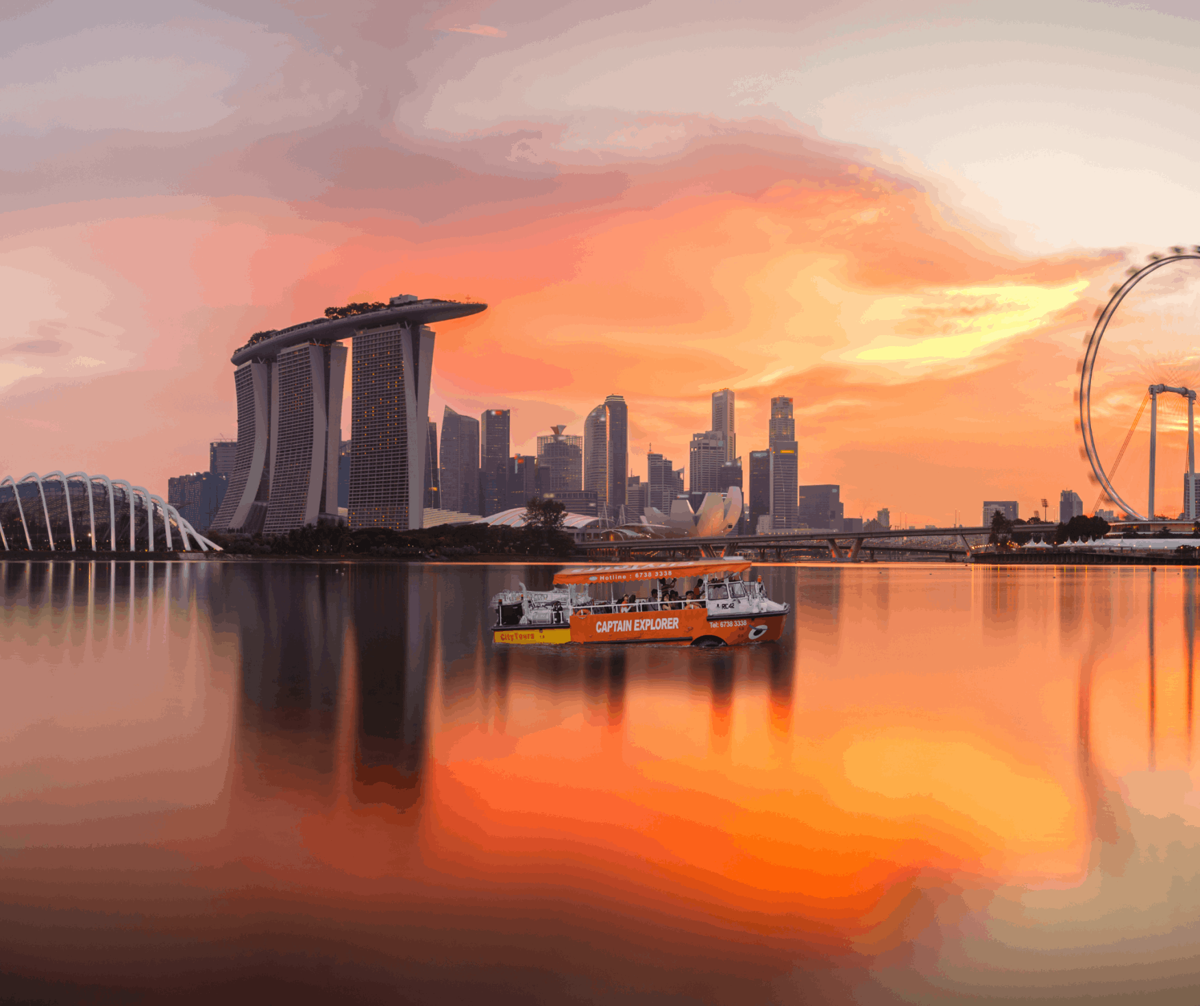 Captain Explorer DUKW tour cruising at sunset in Marina Bay, with Singapore Flyer and Marina Bay Sands skyline in the background.