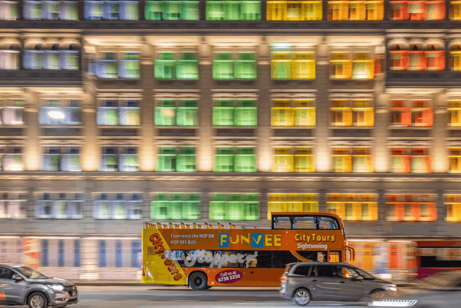 FunVee City Tours hop-on hop-off bus passing by the Old Hill Street Police Station with colourful rainbow windows in Singapore at night