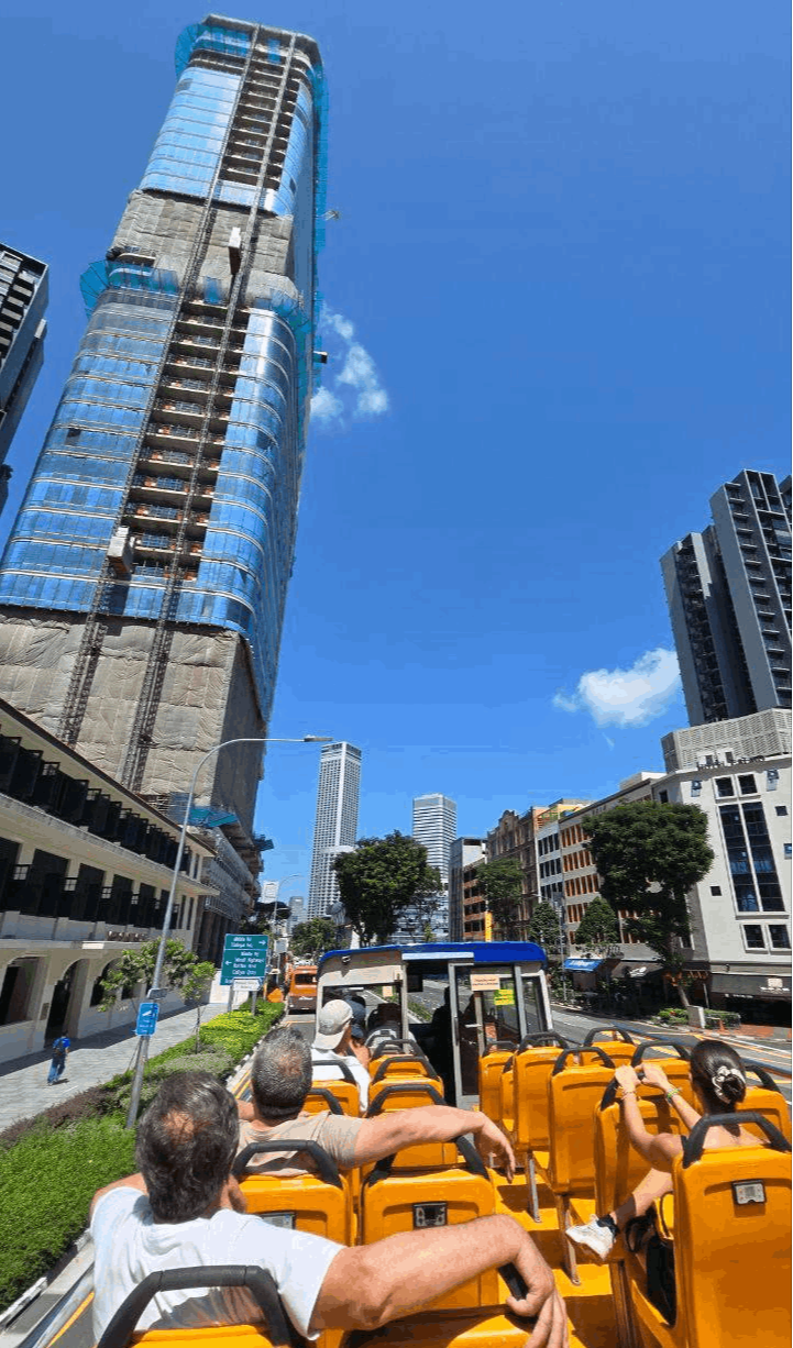 Tourists enjoying a sunny ride on the FunVee Open-Top Bus with views of modern skyscrapers in downtown Singapore.