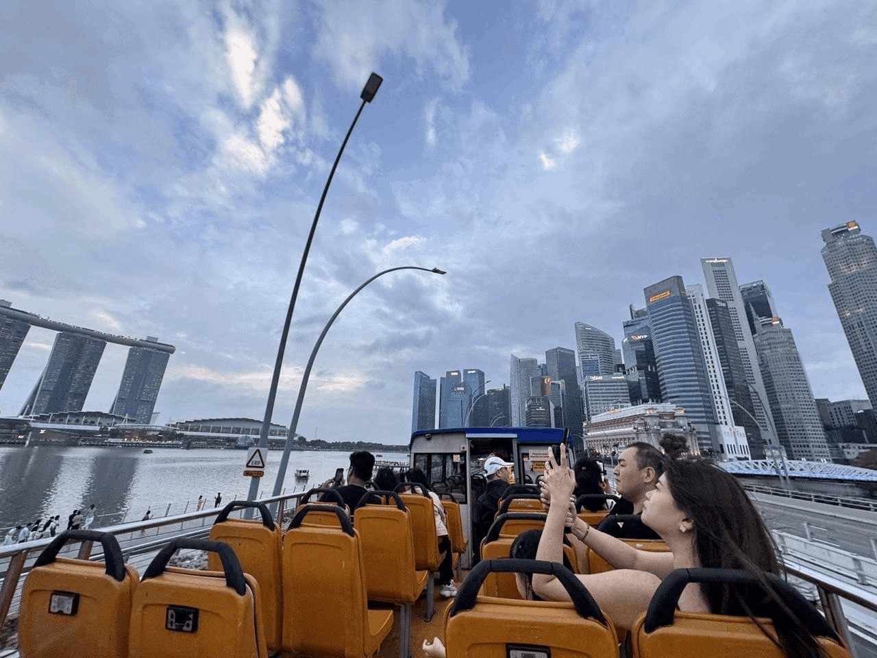 Bright orange FunVee Hop-on Hop-off sightseeing bus driving past Marina Bay – part of the 3-day Singapore Easy Pass itinerary for tourists