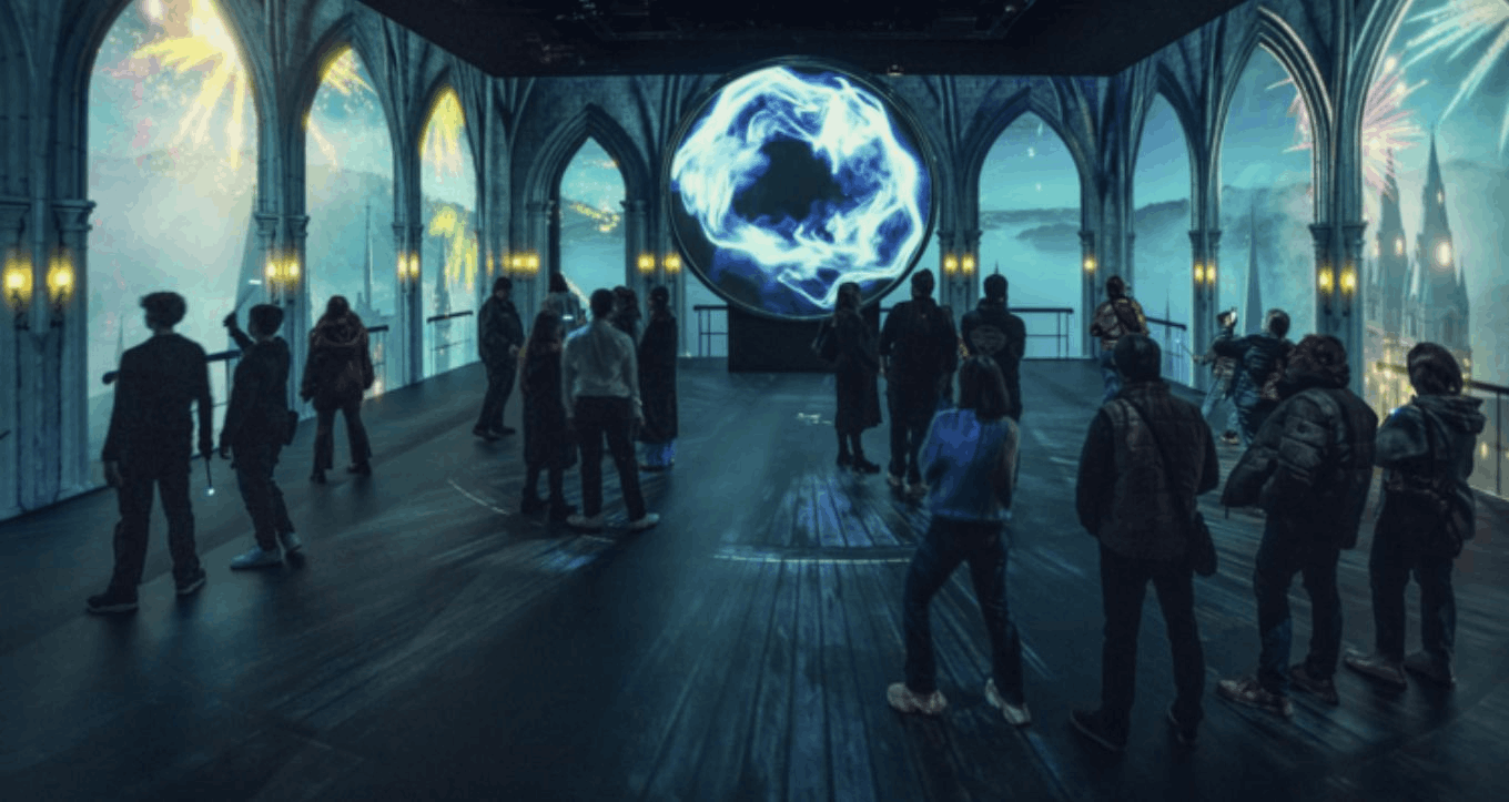 Visitors exploring an immersive Harry Potter-themed room at Resorts World Sentosa, featuring magical light projections, interactive wands, and castle-like arches. colourful storefronts under a large transparent canopy.