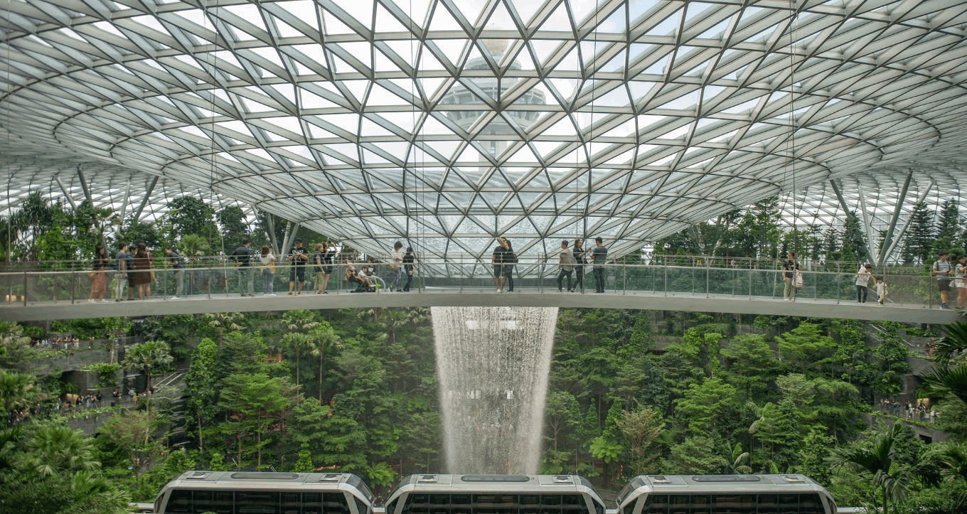 Visitors walking across the sky bridge at Jewel Canopy Park with lush greenery and the world’s tallest indoor waterfall in the background.