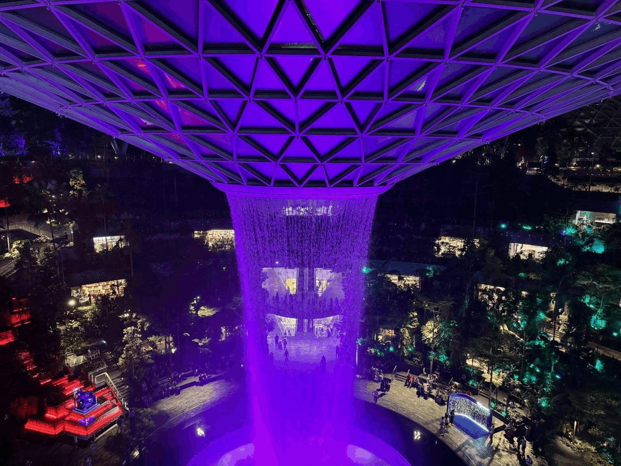The Rain Vortex at Jewel Changi Airport illuminated at night, featuring the world’s tallest indoor waterfall surrounded by lush greenery.