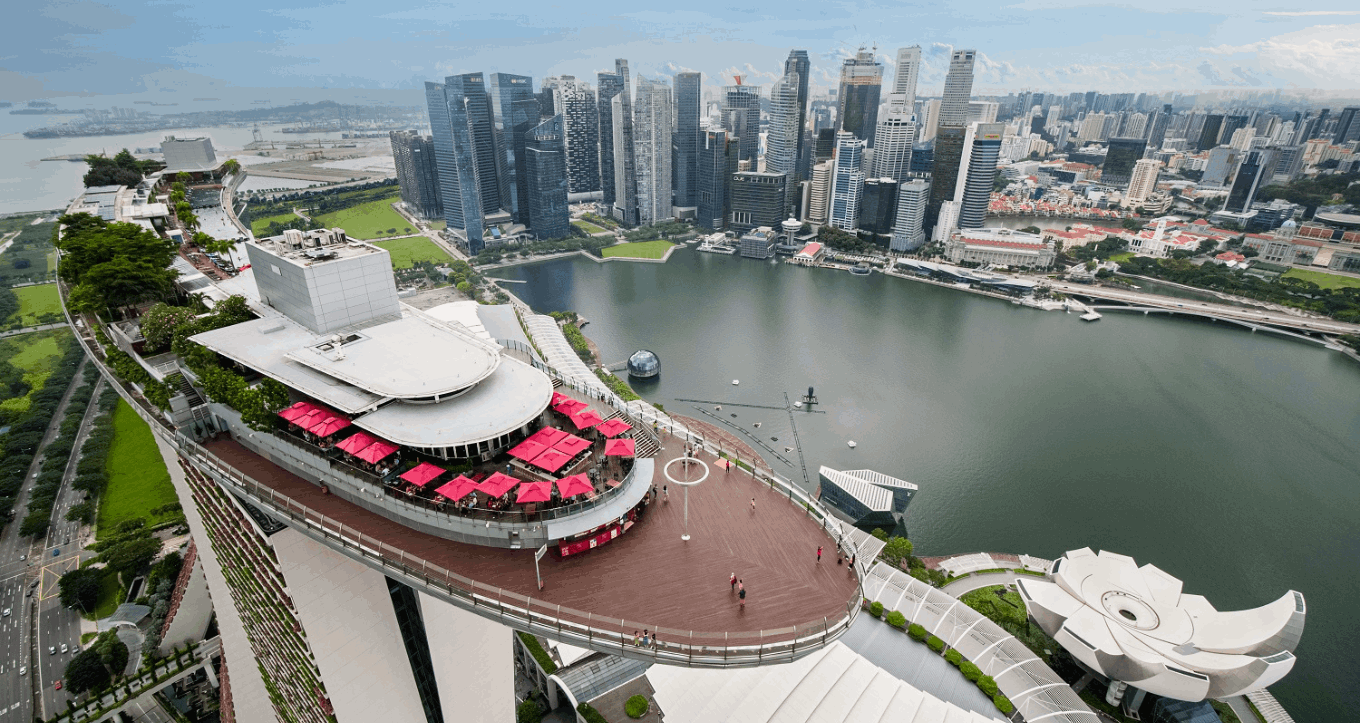  An aerial view of the iconic Marina Bay Sands SkyPark, showcasing its observation deck and infinity pool area, with the Singapore city skyline and bay in the background.