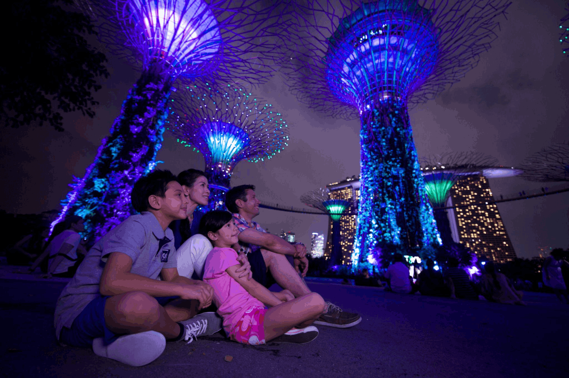 Family watching the illuminated Supertree Grove at Gardens by the Bay, a colourful evening attraction for visitors exploring Singapore at night.