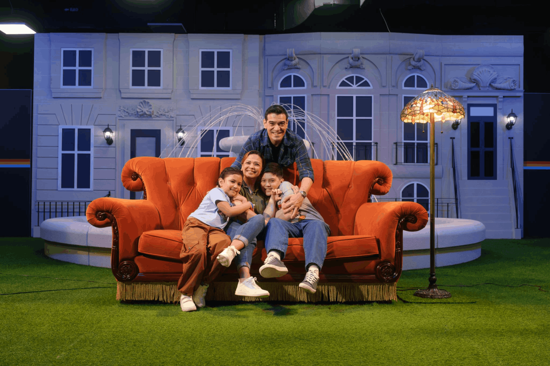 A family posing on the iconic orange velvet couch in front of the fountain at The Friends Experience in Singapore, a top indoor attraction for March 2026.